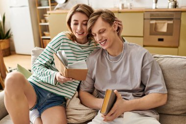 Sevgi dolu bir çift güler ve evde birlikte kitap okurken keyifli bir anı paylaşır..