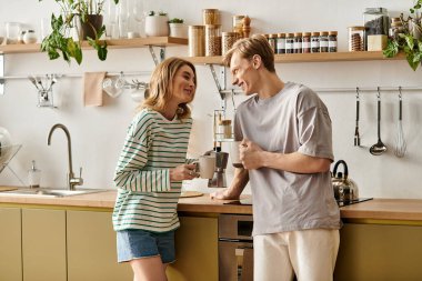 Genç bir çift, kahkaha ve kahveyi modern mutfaklarında paylaşır, sıcaklık ve sevgi saçar..