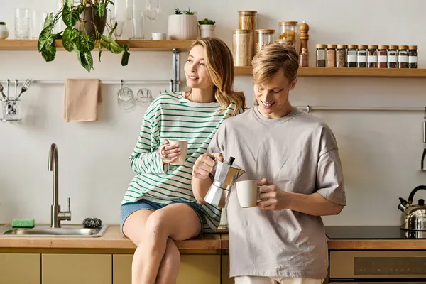 Genç bir çift evlerinde hassas bir anı paylaşıyor, kahvelerini yudumluyor ve mutfaklarında sıcak bir gülümseme sergiliyor..