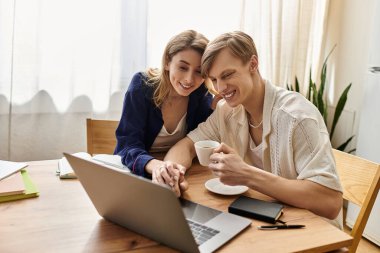 Genç çift, bir dizüstü bilgisayar ve kahve ile birbirlerine bağlanırken şık evlerinde keyifli bir anı paylaşıyorlar..