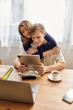 Tarz sahibi genç bir çift, evdeki tablette içeriği incelerken sevgi dolu bir şekilde kucaklaşır..