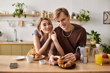 Bir çift, mutfaklarında kruvasan ve kahve ile sıcak bir kahvaltıdan zevk alır..