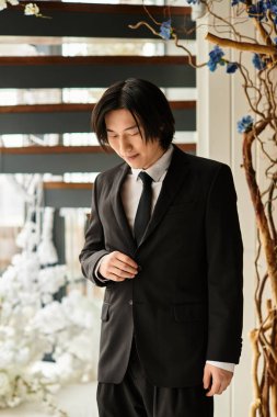 Genç bir damat şık ve neşeli bir düğün salonunda takım elbisesini ayarlıyor..