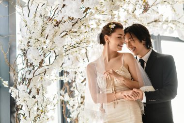 Neşeli gelin ve damat, düğünlerinde beyaz çiçeklerin kucakladığı samimi bir anı paylaşırlar..