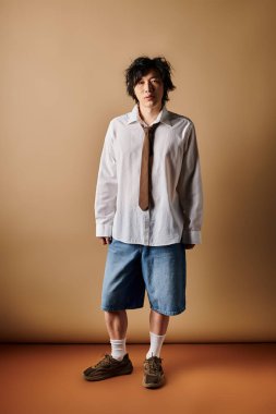 Asyalı bir adam, tarafsız tonlar ve yumuşak ışıklandırmayla süslü bahar kıyafetlerini stüdyoda sergiliyor..