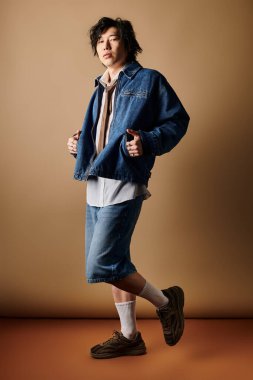 Modaya uygun Asyalı bir adam stüdyo arkaplanının ortasında şık bir bahar elbisesi içinde güven içinde poz veriyor..