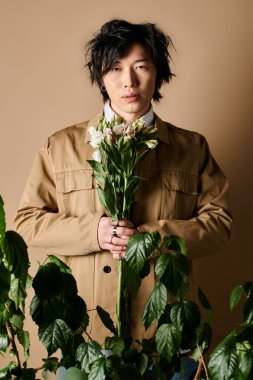 Asyalı adam, bir stüdyoda yeşillik ve çiçeklerle çevrili şık bir bahar görüntüsü sunar..