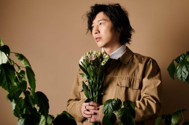 Asyalı bir adam, elinde taze çiçeklerle şık bir bahar elbisesi içinde stüdyoda duruyor..