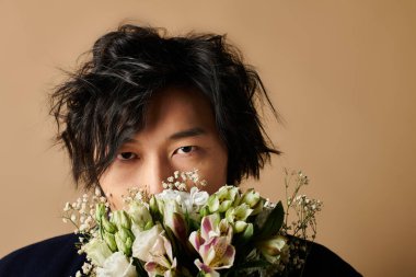 Stüdyoda şık giyinen bir adam bahar temasını tamamlayan çiçekler tutuyor..