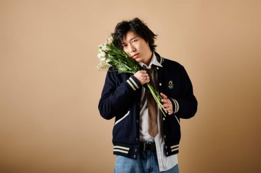 Asyalı şık bir adam çiçeklerle poz verir. Stüdyoda baharın özünü somutlaştırır..