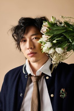 Asyalı bir adam stüdyoda şık bir bahar elbisesi sunuyor, elinde zarif bir şekilde taze çiçekler tutuyor..