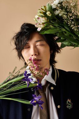 Şık bir Asyalı, taze bahar çiçekleriyle dolu bir stüdyoda düşünceli bir şekilde poz verir..