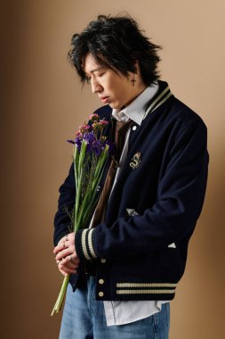 Şık bahar kıyafetleri giymiş Asyalı bir adam modern bir stüdyo ortamında canlı çiçekler tutuyor..