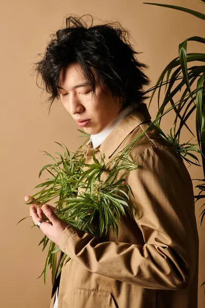 Asyalı bir adam, stüdyo ortamında yeşilliklerle çevrili modaya uygun bahar kıyafetleri modelliyor..