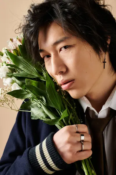 Genç bir adam, stüdyoda zarif bir şekilde taze çiçekleri tutarken modern bahar kıyafetlerini sergiliyor..