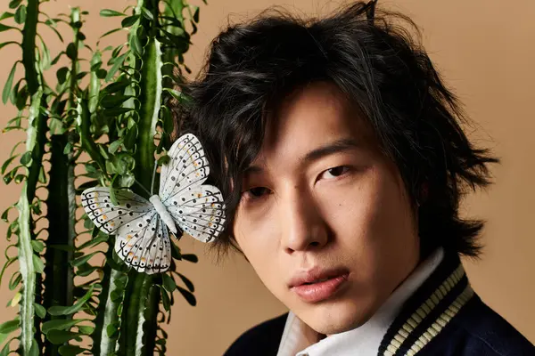 Asyalı bir adam, bitkilerle tamamlanmış sıcak bir stüdyoda bahar modasına uygun kıyafetler sergiliyor..