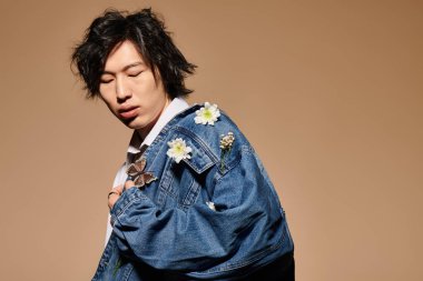 Asyalı bir adam, çiçeklerle süslenmiş bir kot ceketle çağdaş bir bahar kıyafetini modelliyor..