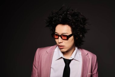 Havalı bahar kıyafetleri giymiş Asyalı bir adam karanlık bir arkaplanda güven içinde poz veriyor..