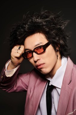 Asyalı bir adam şık bir stüdyo ortamında şık bir bahar elbisesi ve güneş gözlüğü takıyor..