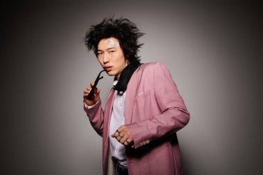 Yüzünde kan olan Asyalı bir adam yaratıcı bir stüdyoda şık bir bahar elbisesi giyiyor.