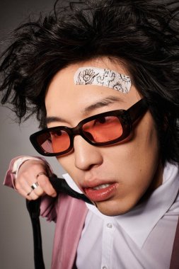 Yüzünde kan olan Asyalı bir adam, modaya uygun bir stüdyoda eşsiz bir moda tarzı sergiliyor.