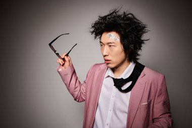 Asyalı bir adam zarif bir şekilde bir stüdyoda poz veriyor, şık bahar moda kıyafetleri sergiliyor..