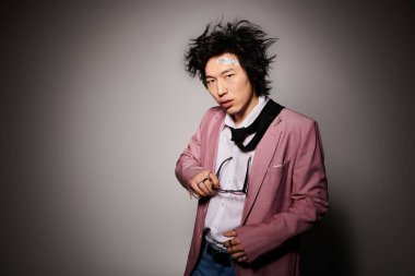 Asyalı bir adam şık kıyafetler içinde canlı bir stüdyo ortamında poz veriyor..