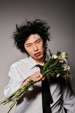 Havalı bahar kıyafetleri içinde yüzünde kan olan modacı bir adam elinde çiçekle rahatça poz veriyor..