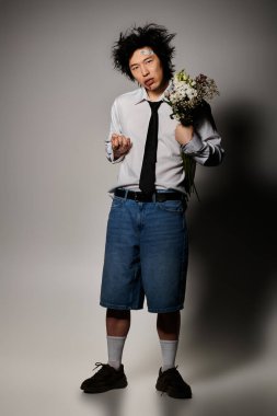 Yüzünde kan olan şık bir Asyalı stüdyoda rahat bir şekilde poz veriyor. Günlük kıyafetleri çiçeklerle harmanlıyor..