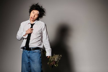 Yüzünde kan olan Asyalı bir adam, yaratıcı bir stüdyoda elinde çiçeklerle şık bahar modasına güvenerek poz veriyor..