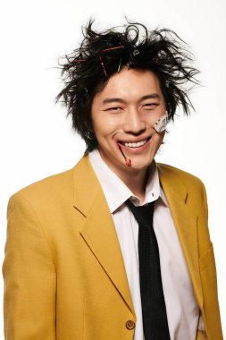 Yüzünde kan olan modaya uyan Asyalı bir adam parlak bir stüdyo ortamında cesur ve seçici bir stil sergiliyor..