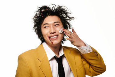 Yüzünde kan lekesi olan Asyalı bir adam stüdyoda cesur moda seçimleri yapıyor ve gülümsüyor.