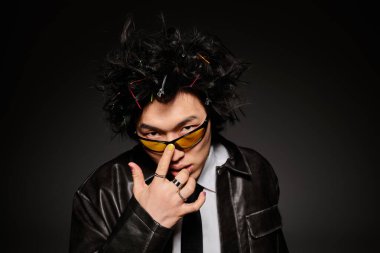 Moda kıyafetleri giymiş Asyalı bir adam karanlık bir arka plana karşı stüdyoda güven içinde poz veriyor..