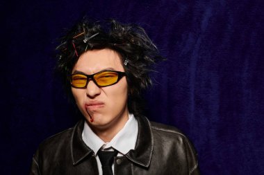 Yüzünde kan olan hoşnutsuz Asyalı bir adam şık stüdyo kıyafetlerinde eşsiz bahar moda trendleri sergiliyor..