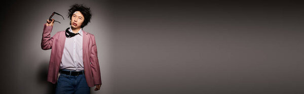 An asian man with blood on face displays fashionable spring attire in a stylish studio setting, exuding confidence, banner