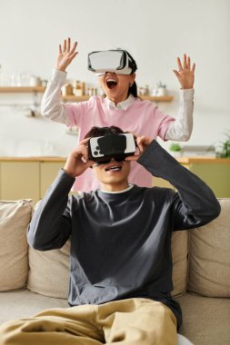 Evde genç bir çift sanal gerçeklik eğlencesi yapıyor, neşe ve kahkaha paylaşıyorlar..