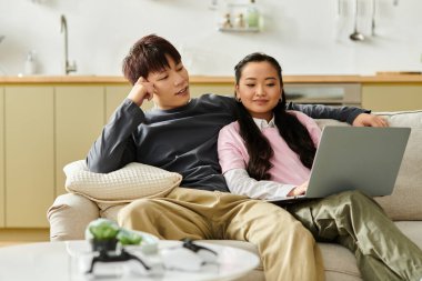 Genç bir Asyalı çift kanepede dinleniyor, dizüstü bilgisayar kullanırken kahkaha ve düşüncelerini paylaşıyorlar..