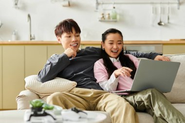 Genç bir çift kanepede rahatça oturur, bir dizüstü bilgisayarla çalışırken gülüşür ve güler..