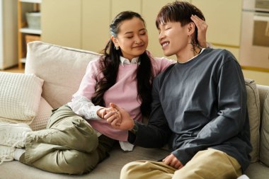 İki genç yetişkin sıcak bir atmosferde sıcak bir kanepede gülüp el ele tutuşuyorlar..