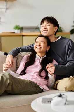 Genç Asyalı bir çift rahat bir öğleden sonranın tadını çıkarır. Rahat bir kanepede gülüp kaynaşırlar..