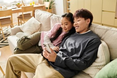 Çift, rahat bir yaşam alanında akıllı telefonlarıyla büyülenmiş bir şekilde koltukta keyifli bir anı paylaşıyor..