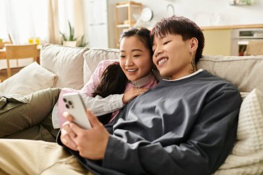 Genç bir Asyalı çift, birlikte eğlenmekten zevk alır. Telefona bakarken gülümserler..