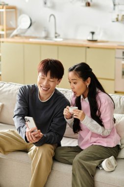 Genç çift evde akıllı bir telefona bakarken birlikte eğlenceli bir anın tadını çıkarıyor..