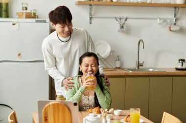 Genç Asyalı bir çift kahvaltıda birlikte gülüyor, evdeki basit mutluluğun tadını çıkarıyorlar..