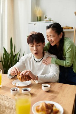 Genç bir Asyalı çift kahvaltısını evde yapıyor, birlikte hamur işlerinin ve içkilerin tadını çıkarıyor..