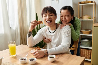 Genç Asyalı bir çift evde keyifli bir kahvaltı yapar, gülümsemelerini ve yemeklerini paylaşırlar..