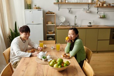 Genç bir çift, gülücükler ve taze meyvelerle dolu evde keyifli bir kahvaltı yapıyor..