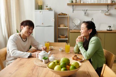 Genç bir çift kahvaltıdan zevk alıyor, gülümsemelerini ve lezzetli yemeklerini evlerinde paylaşıyorlar..