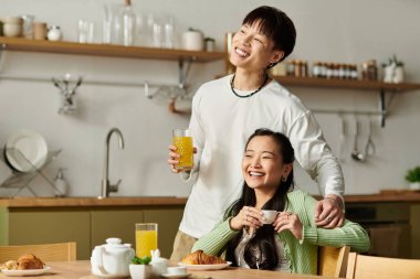 Genç bir Asyalı çift birlikte keyifli bir kahvaltı yapıyor, gülüyor ve içkilerini paylaşıyor..