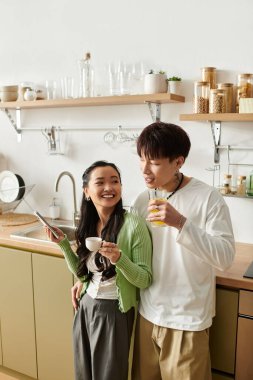 Parlak bir mutfakta, genç bir çift gülümser ve kahvaltıda içkilerini paylaşır..